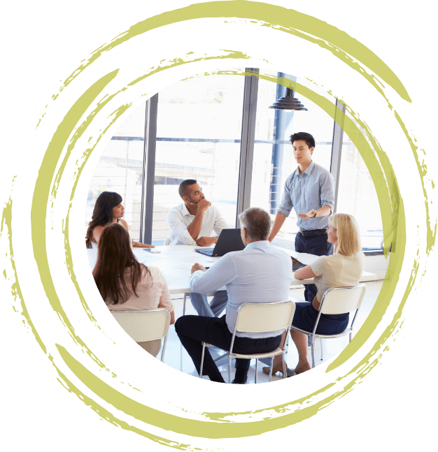 A picture of a man giving a presentation in front of people sitting at a table