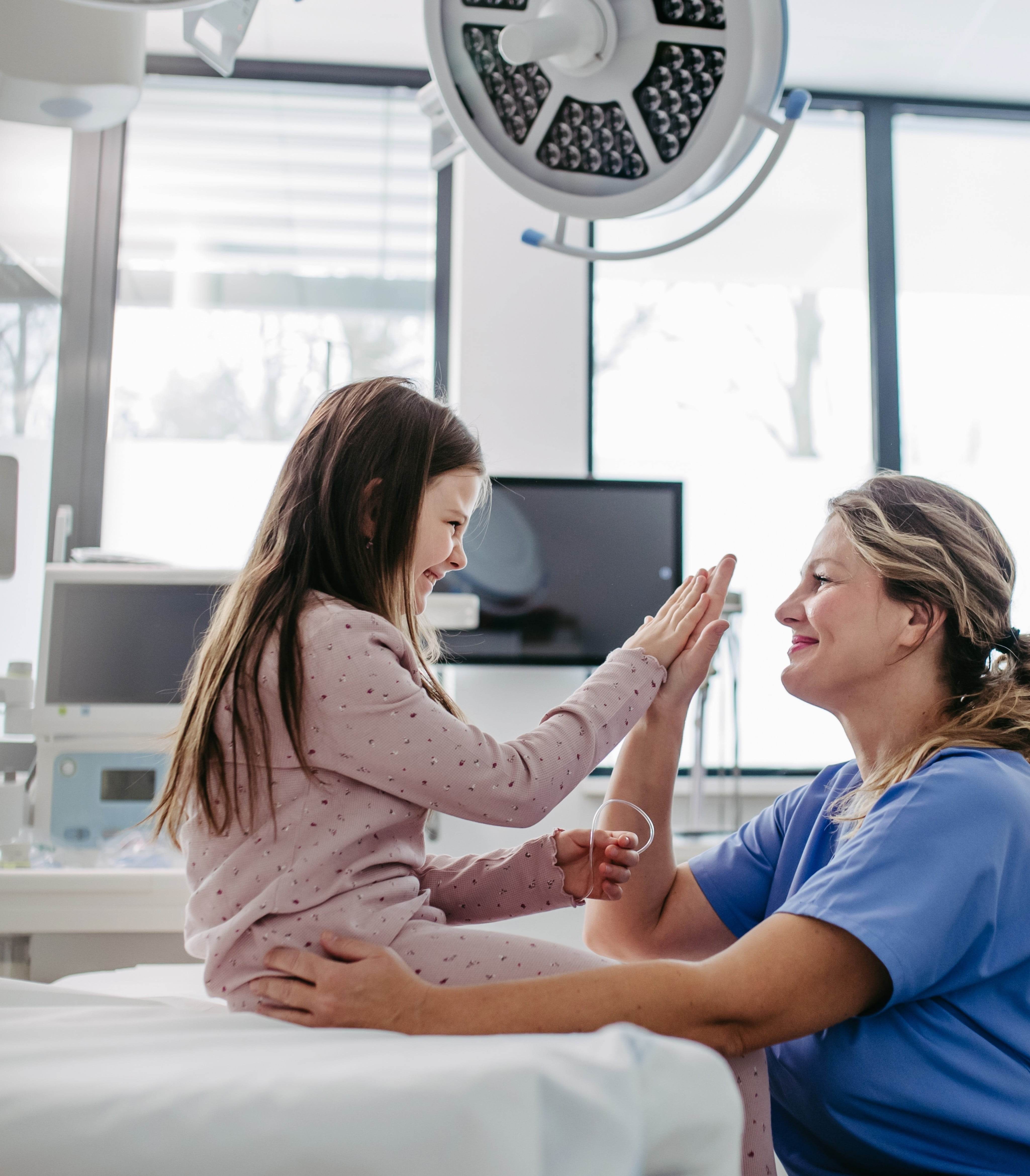 A doctor giving a high five to a little girl on a medical bed.