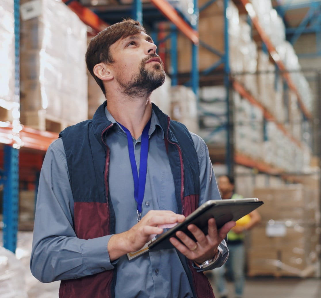 A man inside a warehouse with a iPad open looking up at the shelves inside the warehouse.